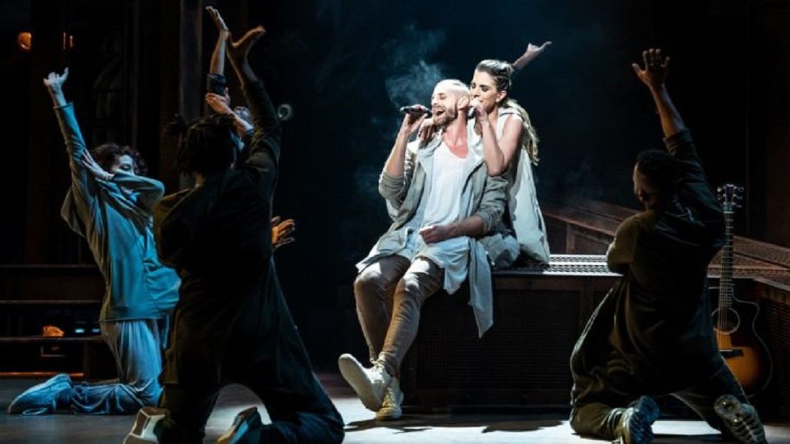 Theatre stage performance with singer kneeling and other performers raising arms in Calgary producti.