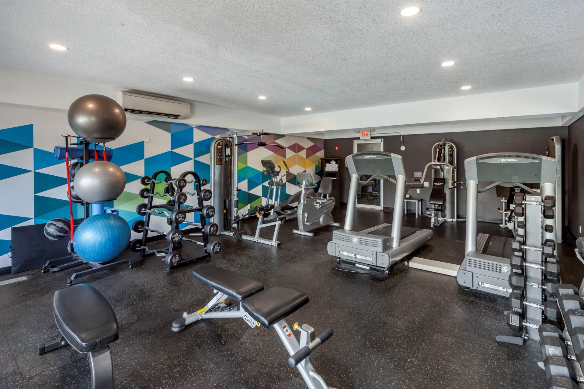 Brightly lit gym with geo pattern blue/green/purple/yellow wallpaper and various equipment