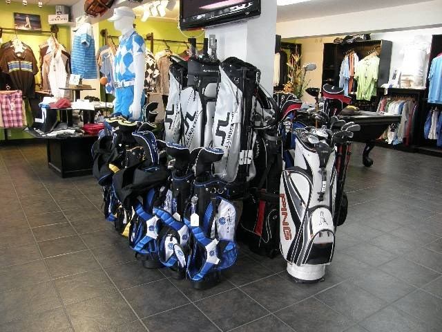 Golf pro shop with bags, clubs, and apparel neatly displayed under bright lighting.