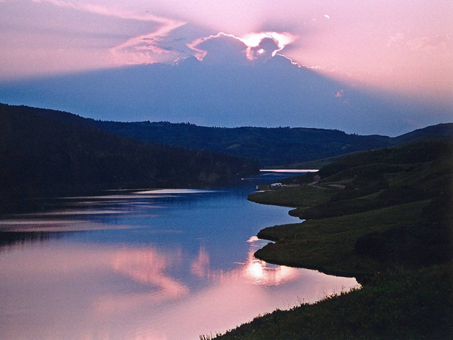 Sunset over calm water with pink and purple sky and green shoreline.