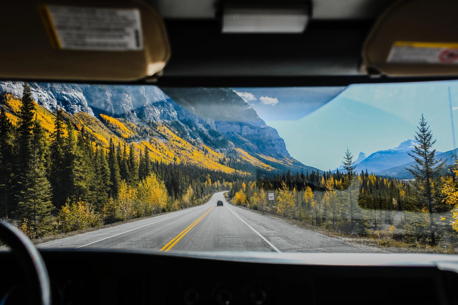 Mountain highway winds through evergreen forest and yellow foliage, viewed through a windshield.