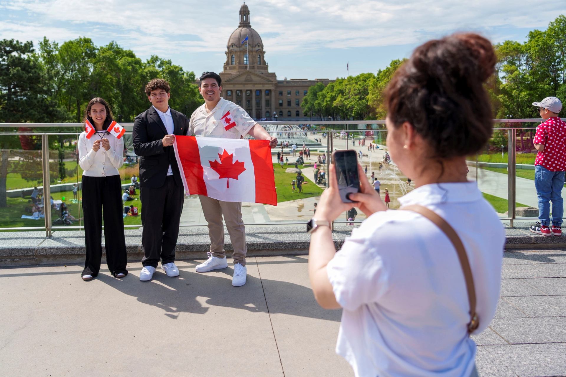 People holding Canadian flags pose for a photo near a government building.