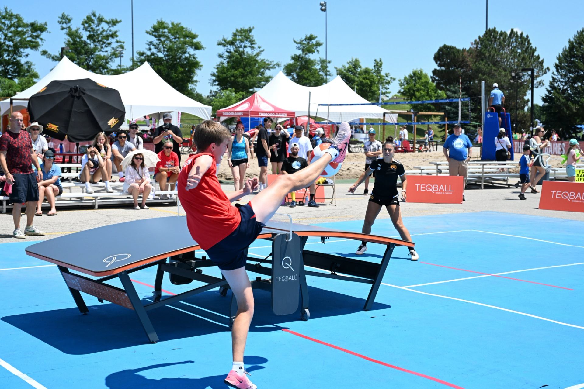 Players kick ball on curved table at The Good Games outdoor event.