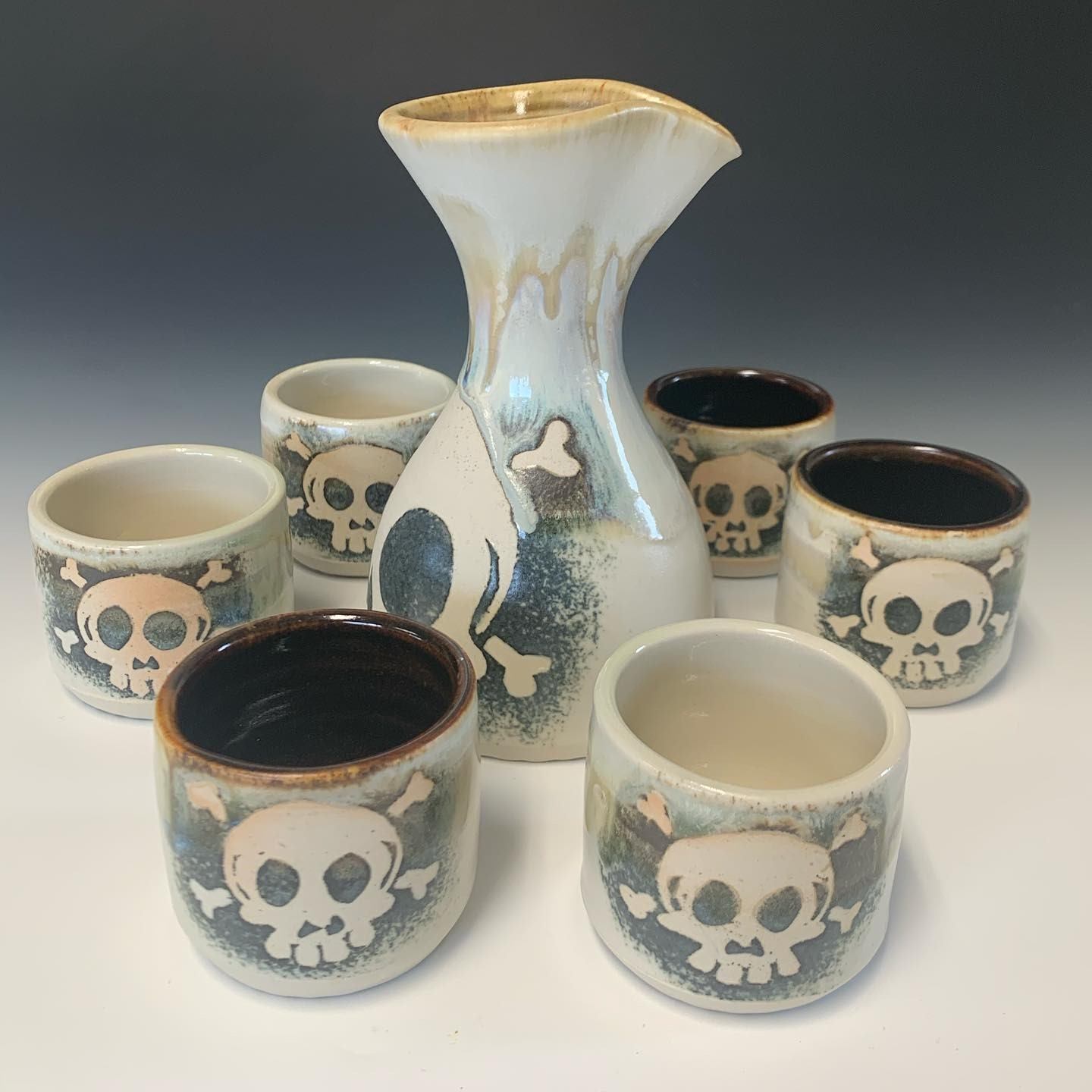 Ceramic carafe and cups with skull-and-crossbones designs on white tabletop.