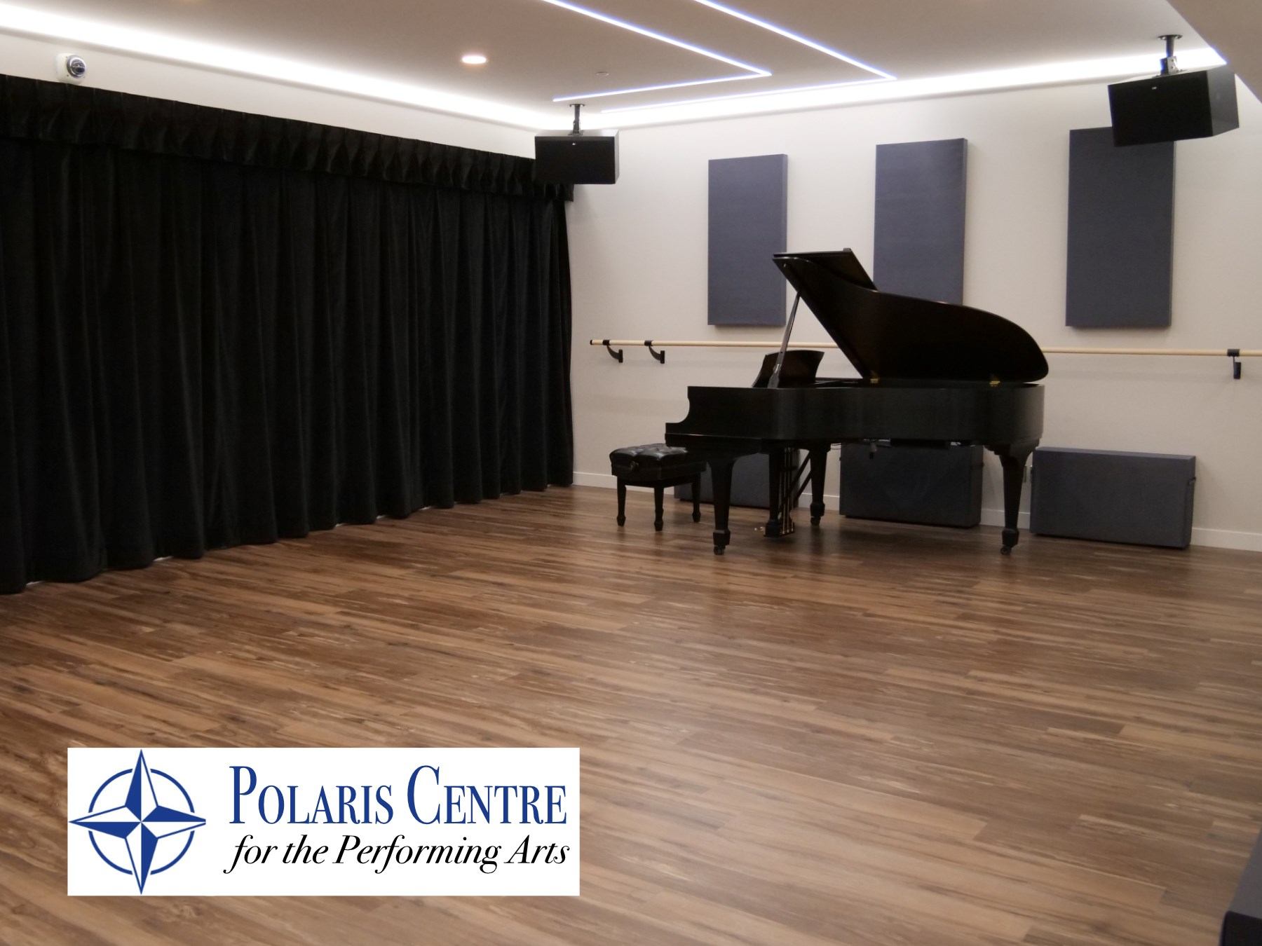 Grand piano in a studio with wood floors, black curtains, and acoustic panels at Polaris Centre.
