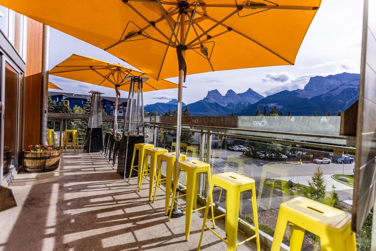 Outdoor patio with yellow umbrellas, stools, and mountain views.