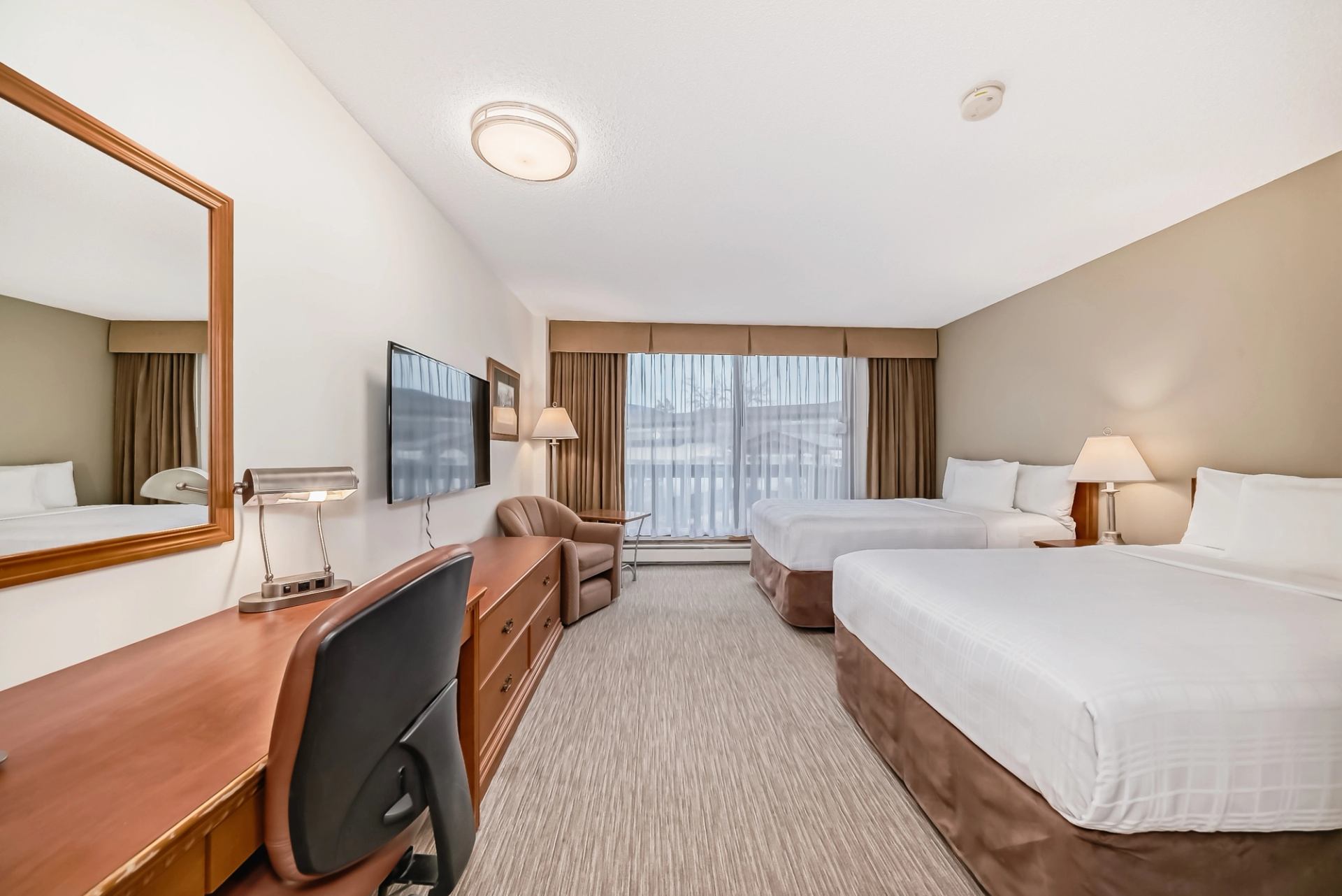 Hotel room featuring two beds, a work desk, armchair, and large window with curtains