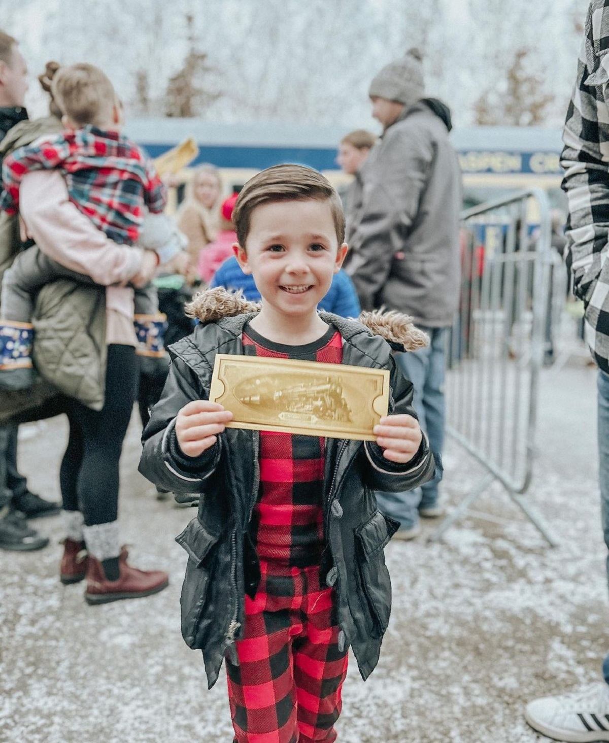 A little boy awaits to board the train with his golden ticket wearing black and red checkered pjs.