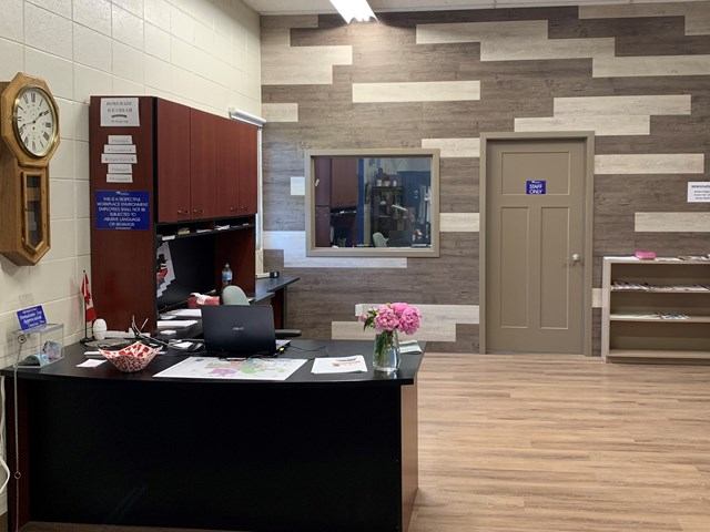 Reception area with desk, clock, flowers, and wooden wall panels.