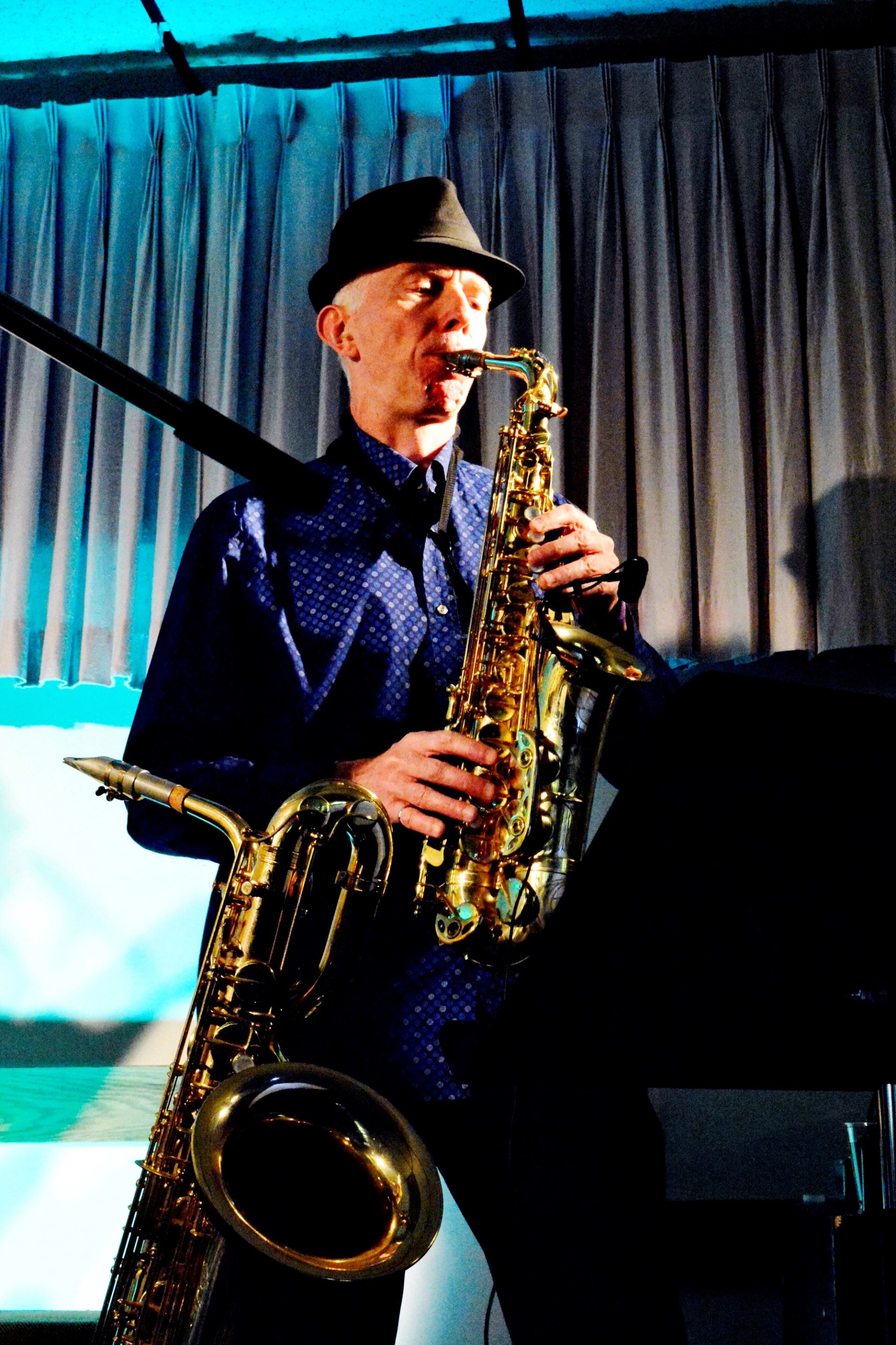Person playing a saxophone on stage under blue lighting.