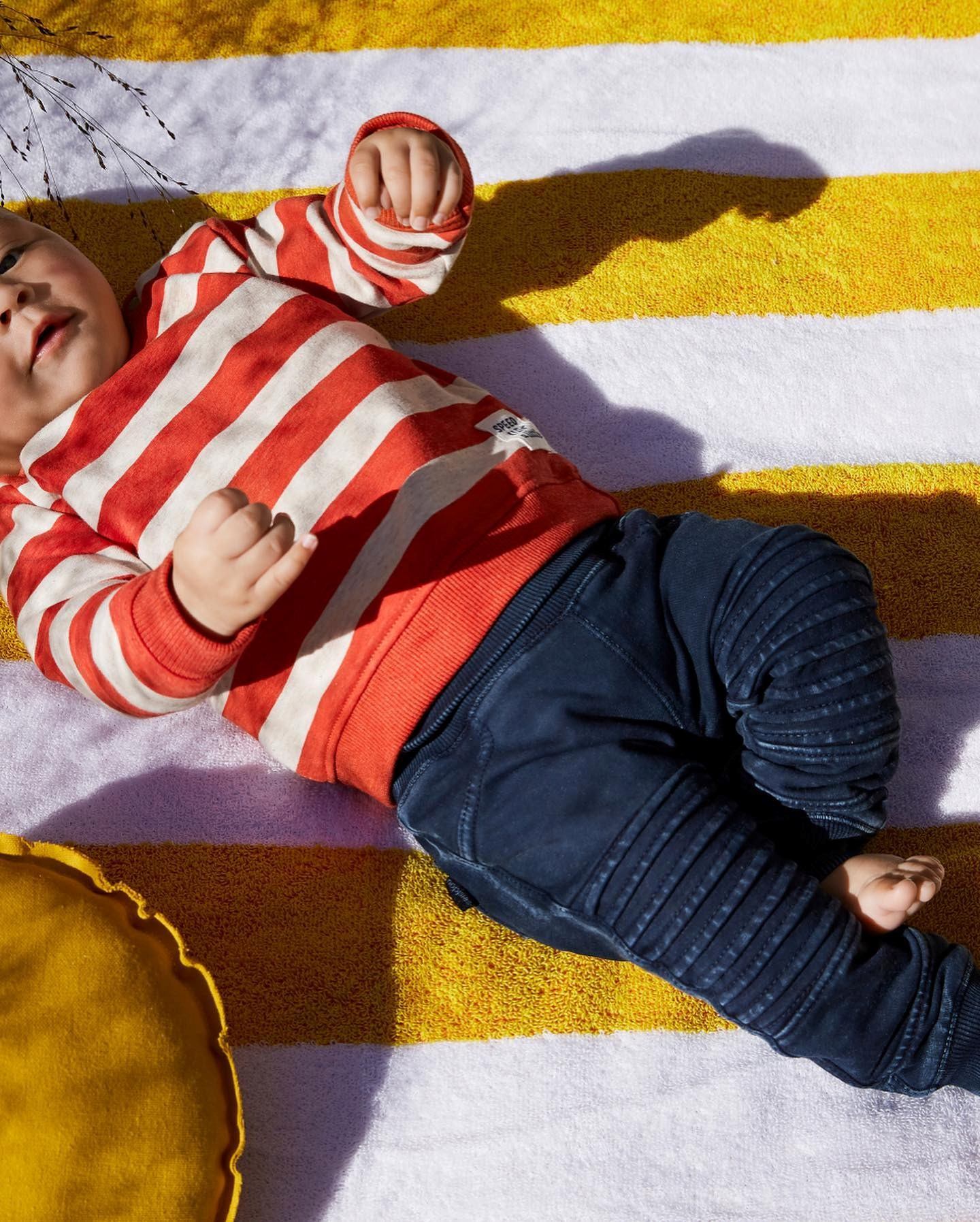 Striped red-and-white hooded baby outfit and navy pants on colorful striped rug.