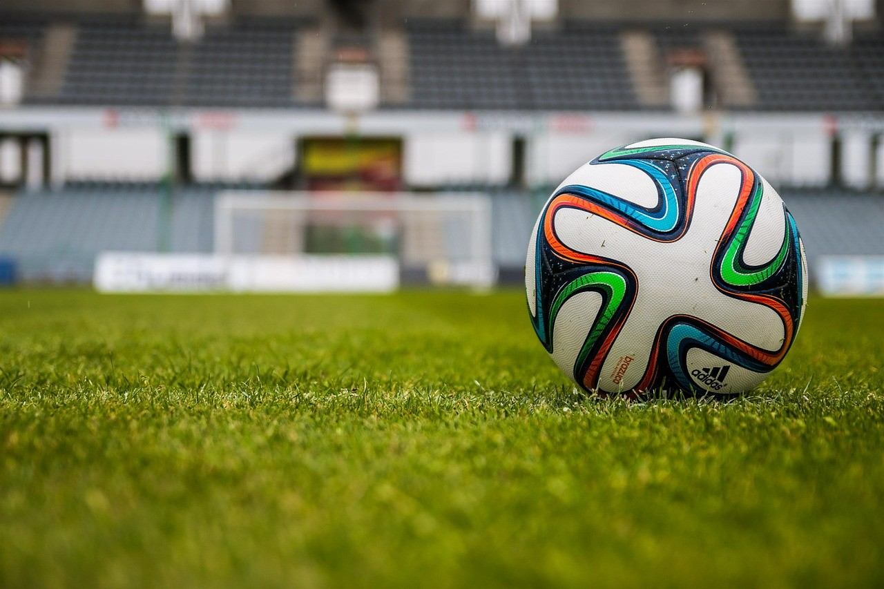 Soccer ball on green grass in front of stadium seating at Ivor Dent Sports Park.