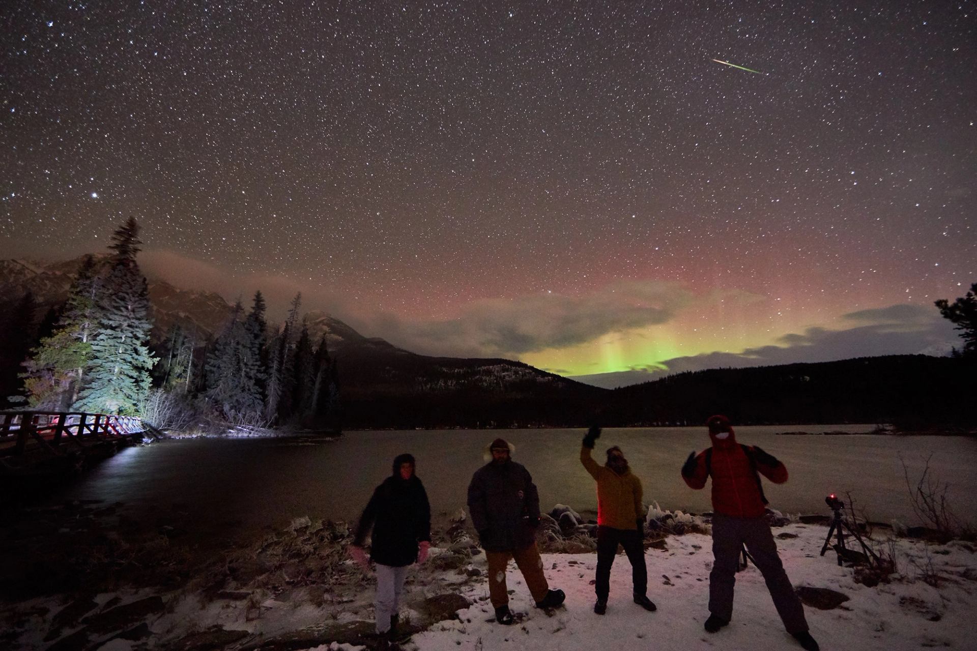 Group of people standing under a starry night sky with aurora borealis in the background.