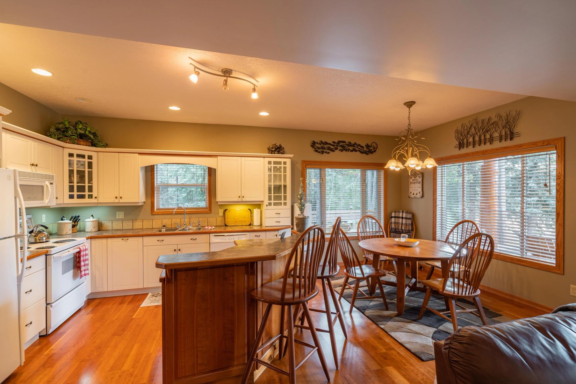 Kitchen with white cabinets, island, pendant lights, dining table, and wood chairs.