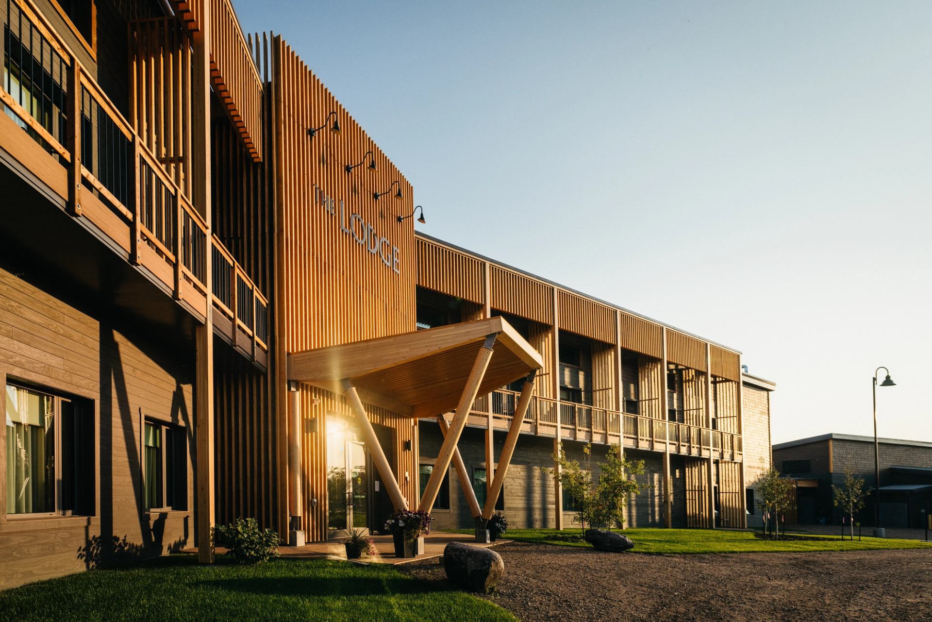 Wooden lodge exterior with covered entrance, balconies, green lawn and clear sky.
