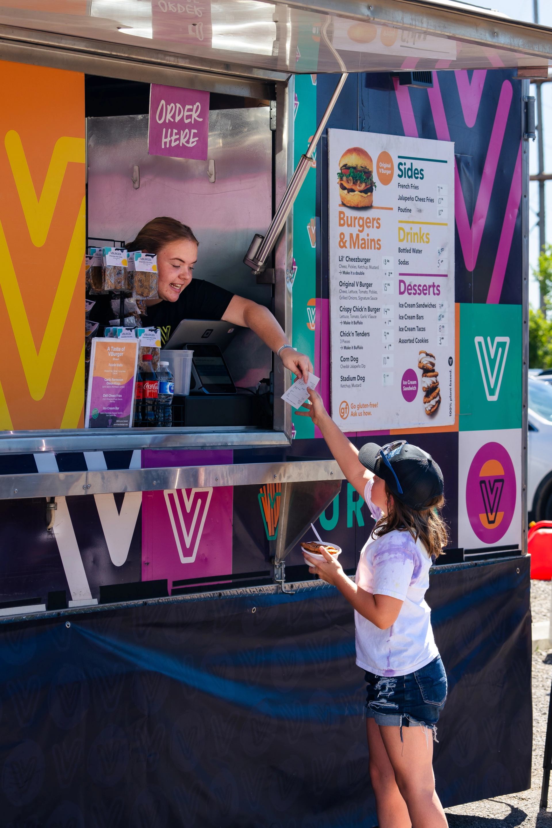 A child reaching up to take her food from the lady in the food truck.