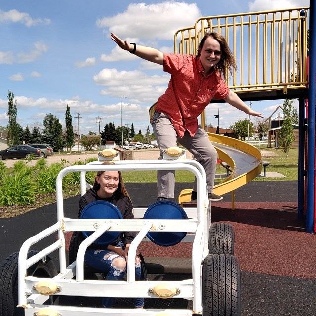 Playground slide and ride car at Mayerthorpe Public Library, with two people outdoors.