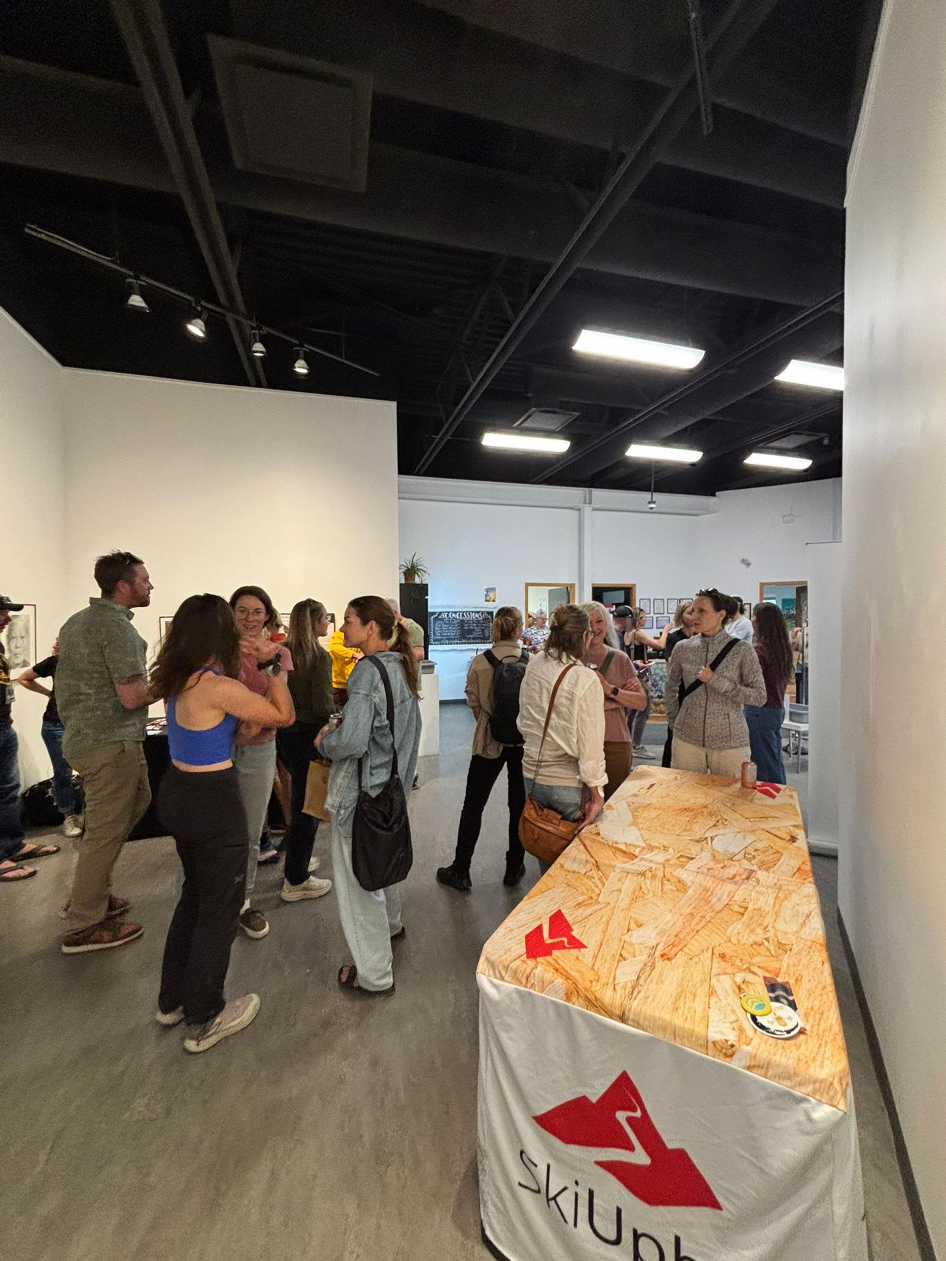 Festival attendees gather, talk, and browse displays in a bright gallery space.