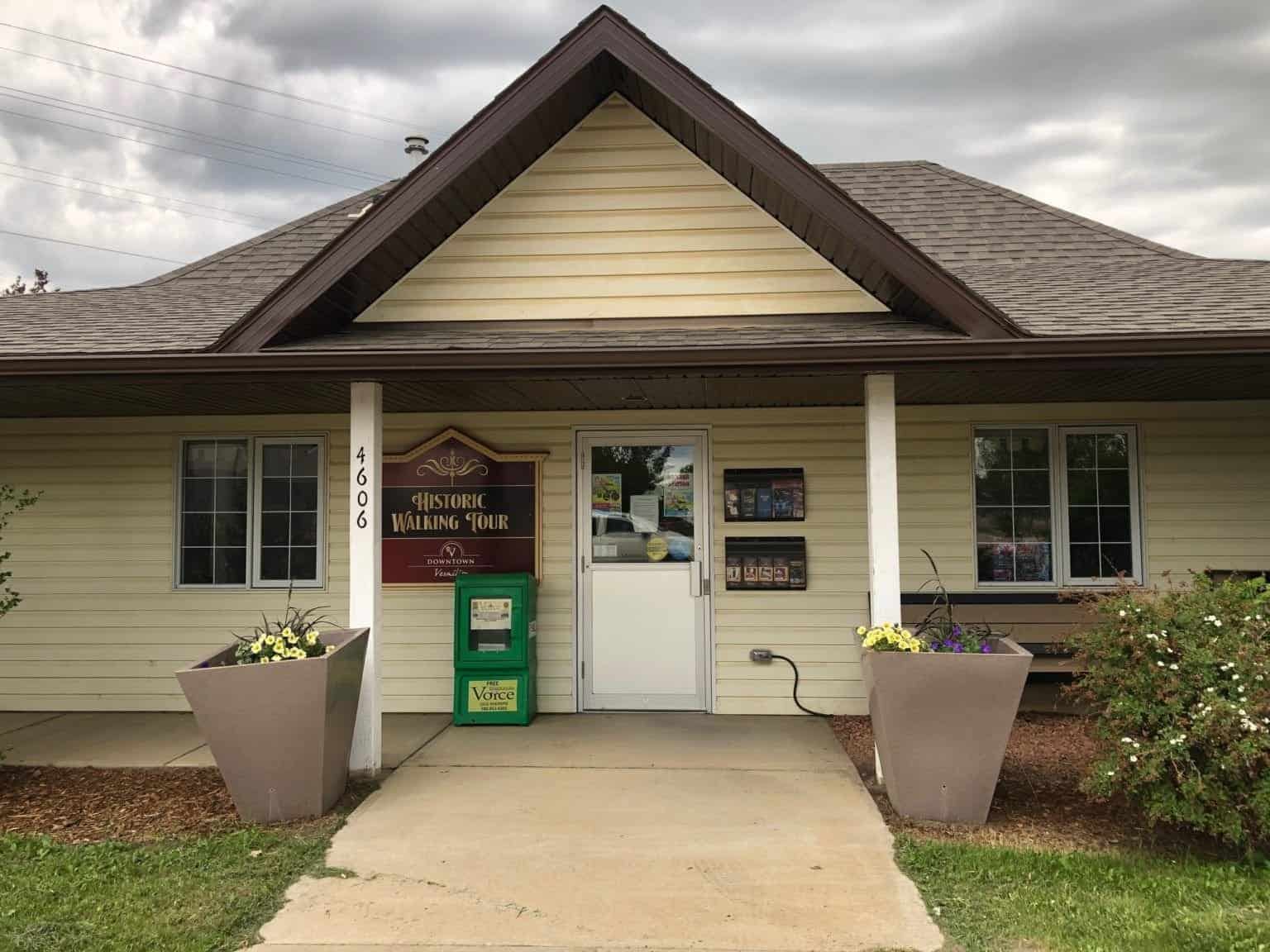 Small beige building entrance with Historic Walking Tour sign, planters and brochure racks