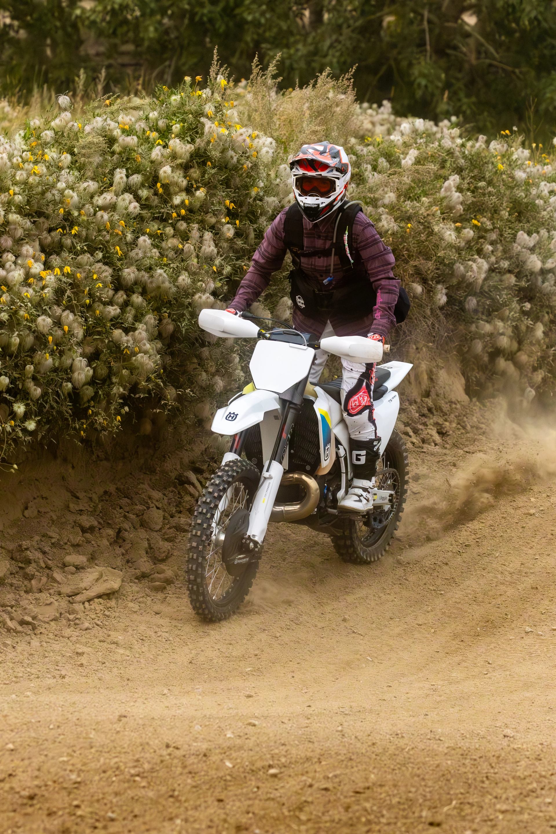Rider on white dirt bike speeding through a forest trail.
