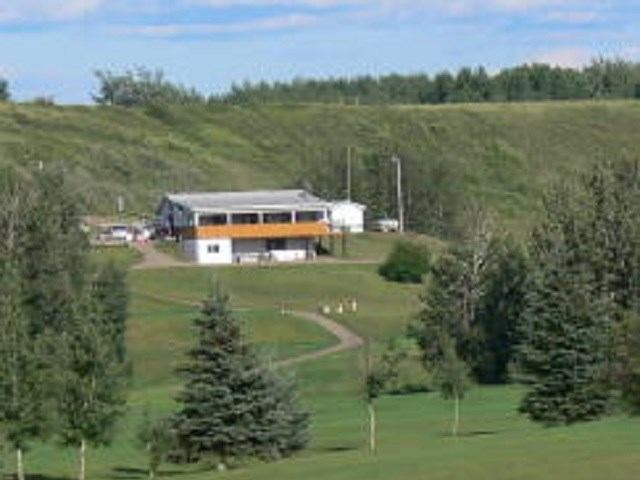 Clubhouse on a green hill with golf carts, trees, and rolling landscape.