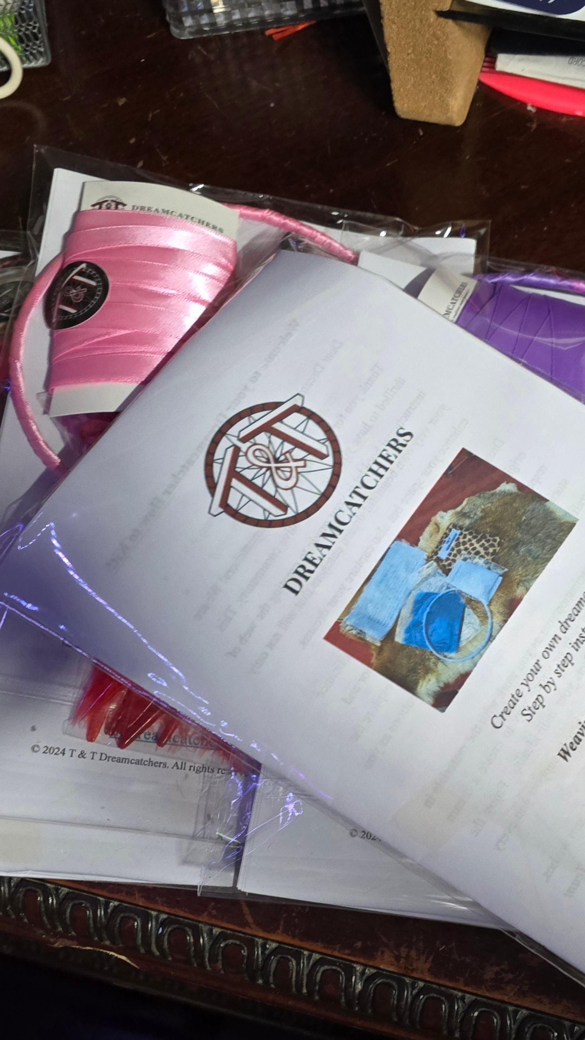 Dreamcatcher craft kit with T & T Dreamcatchers booklet and pink ribbon on table.