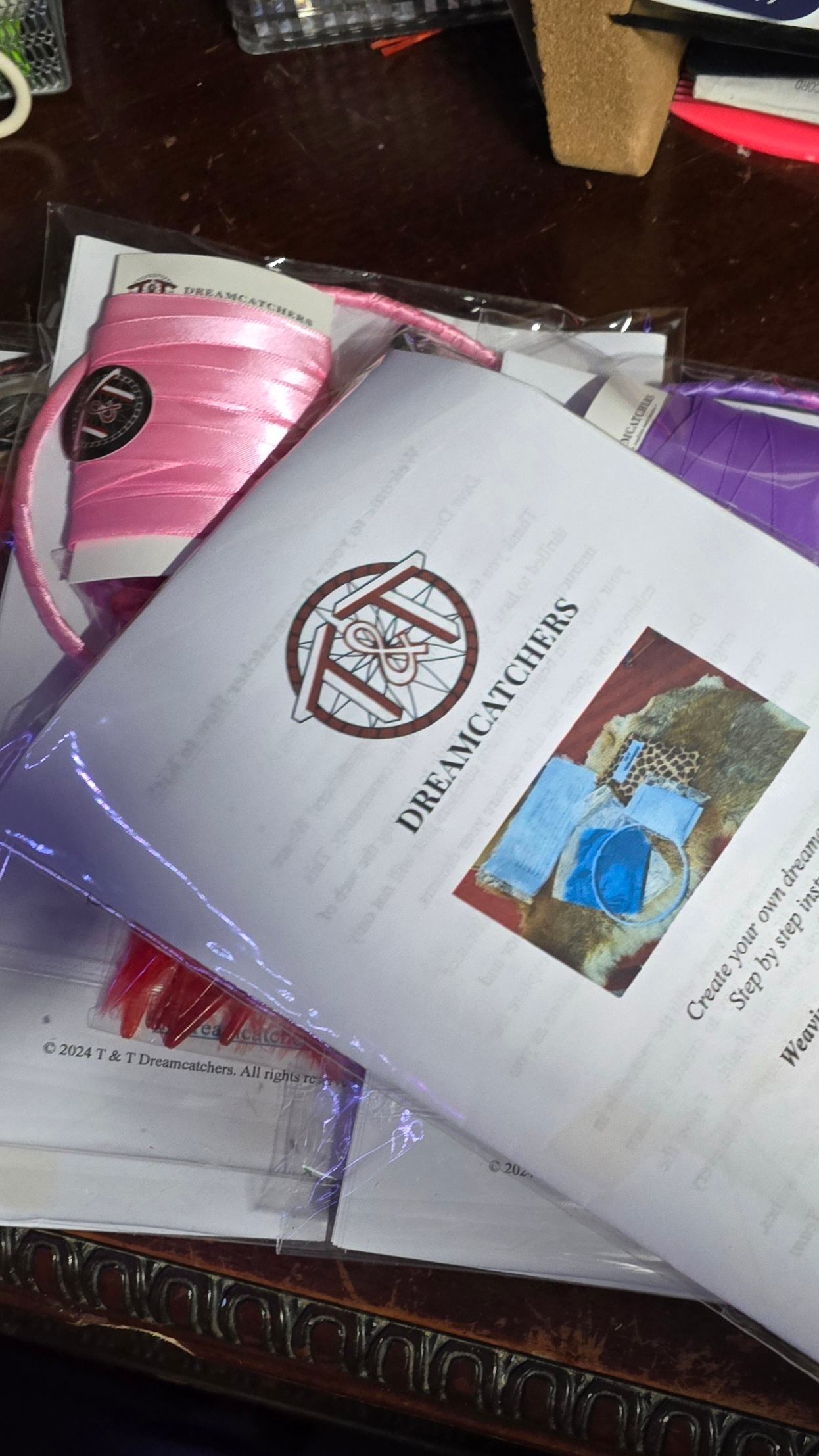Dreamcatcher craft kit with T & T Dreamcatchers booklet and pink ribbon on table.