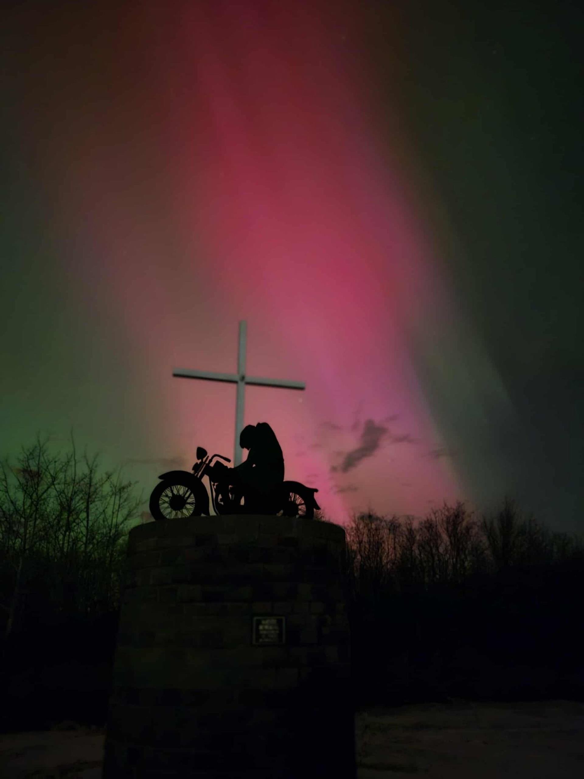 Motorcycle memorial silhouette beneath vibrant aurora colors