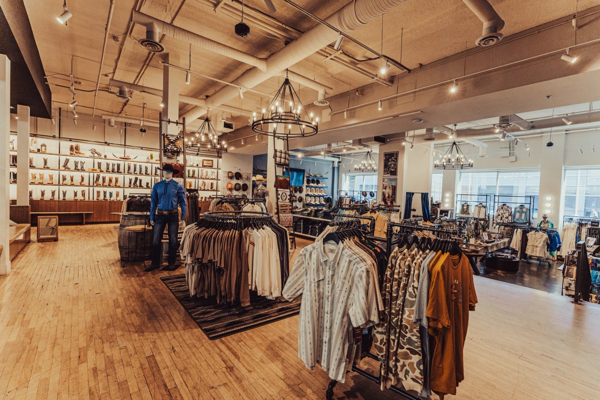Clothing store interior with racks of shirts, cowboy boots on shelves, and decorative lighting.