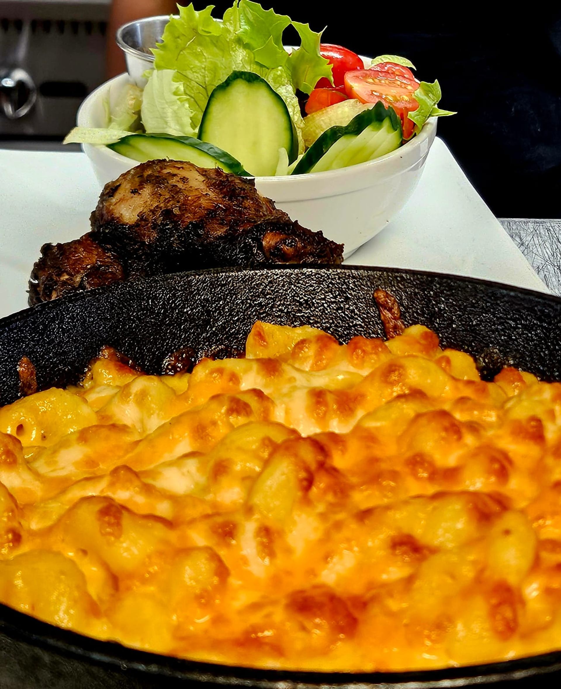 Baked macaroni and cheese with grilled meat and a lettuce, cucumber and tomato salad.