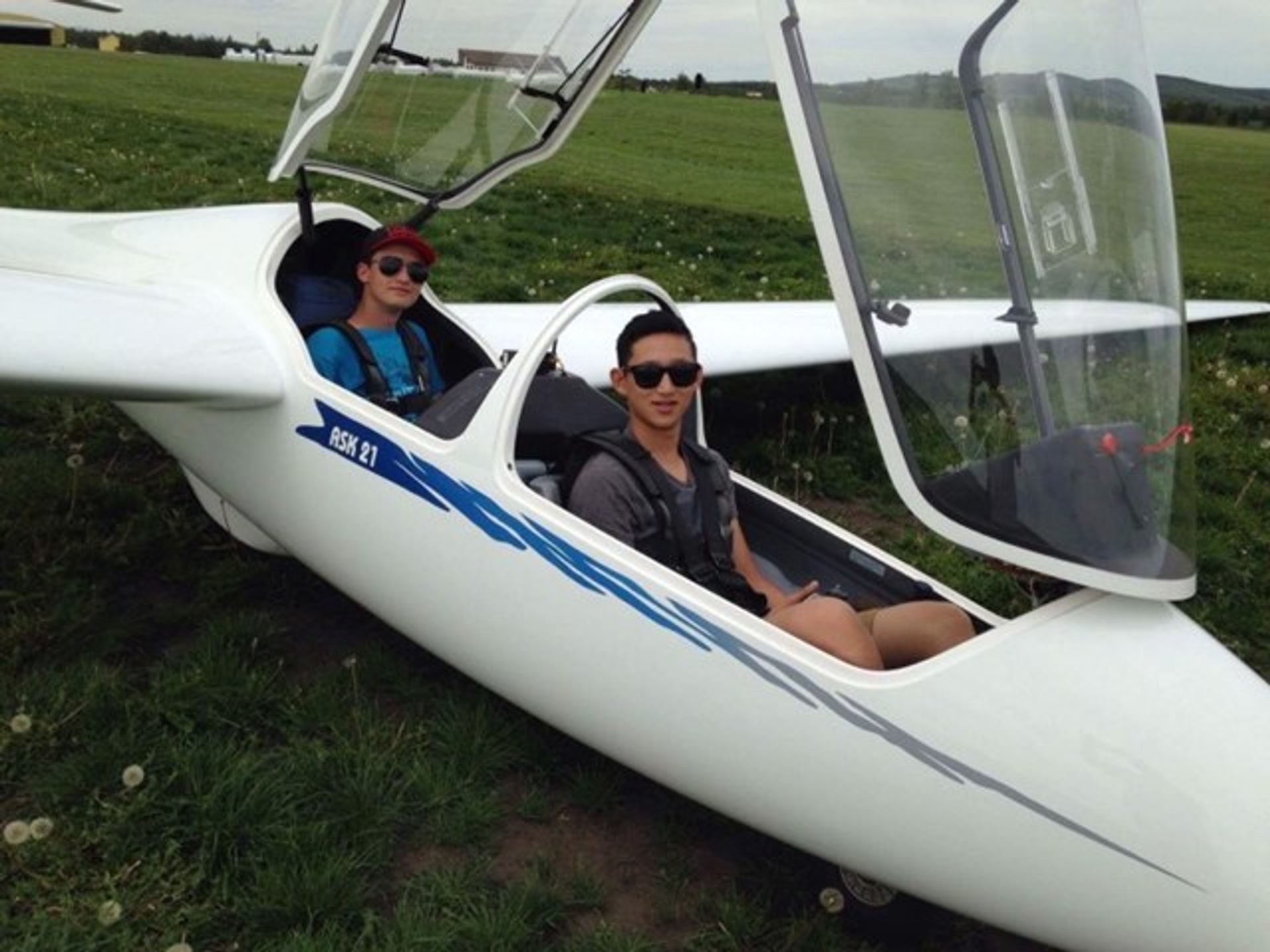 Two-seat white glider on grassy field with open canopy, ready for flight.