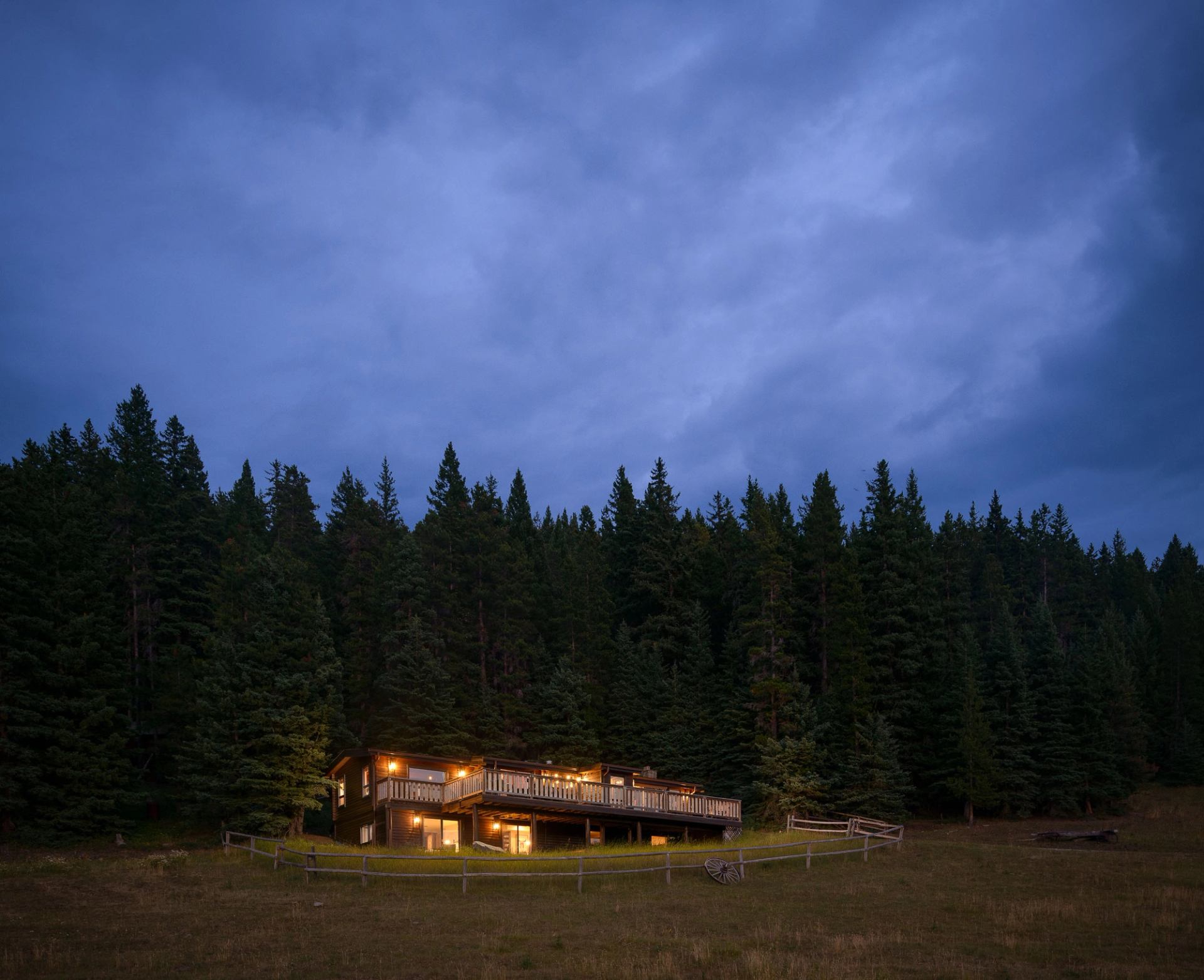 Cabin with warm lights nestled among tall pine trees under a twilight sky.