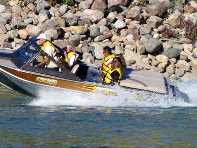 Four people in life vests ride a motorboat along a rocky shore.