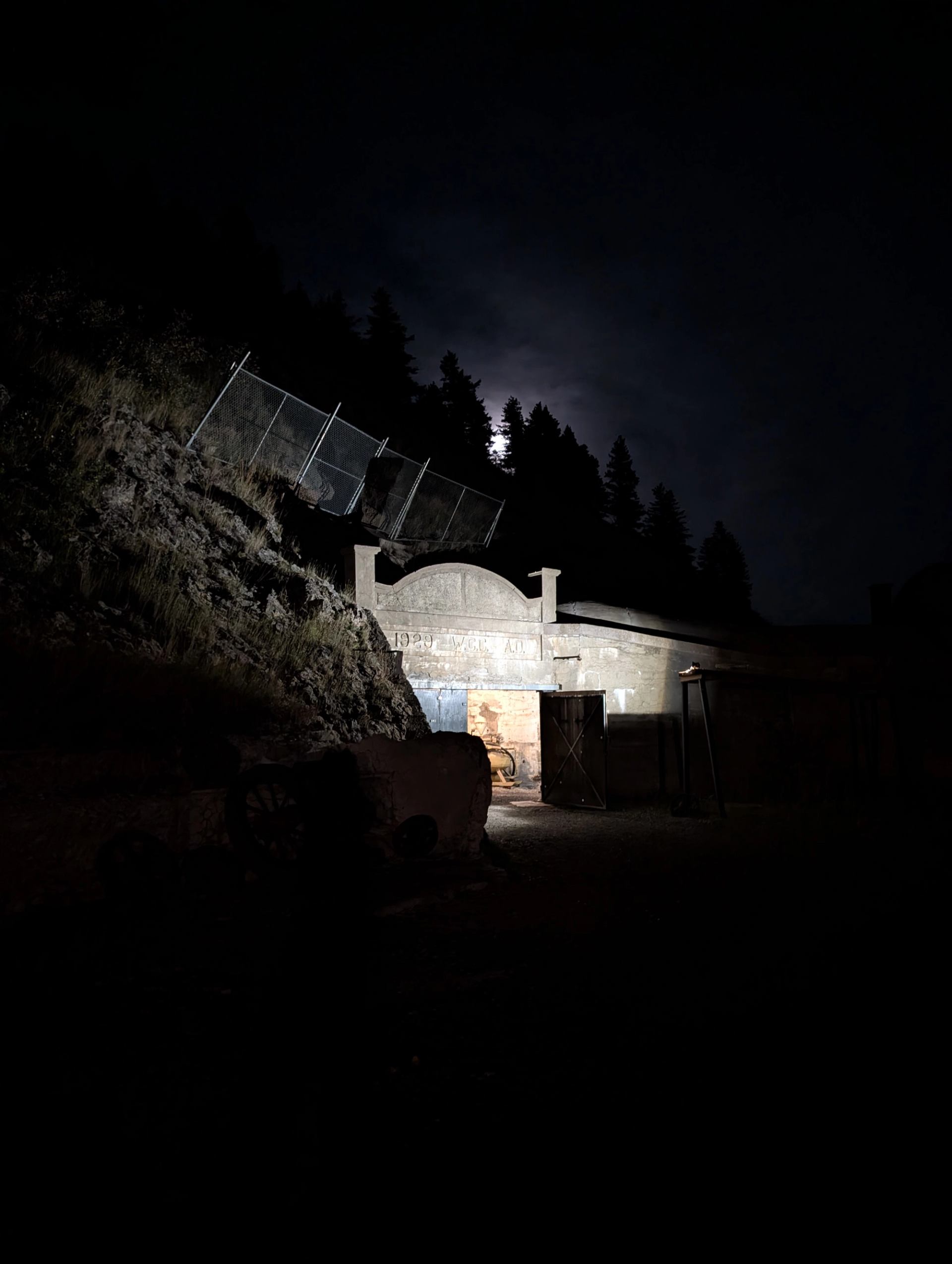 Dimly lit entrance to Bellevue Underground Mine at night with rugged hillside and fencing.