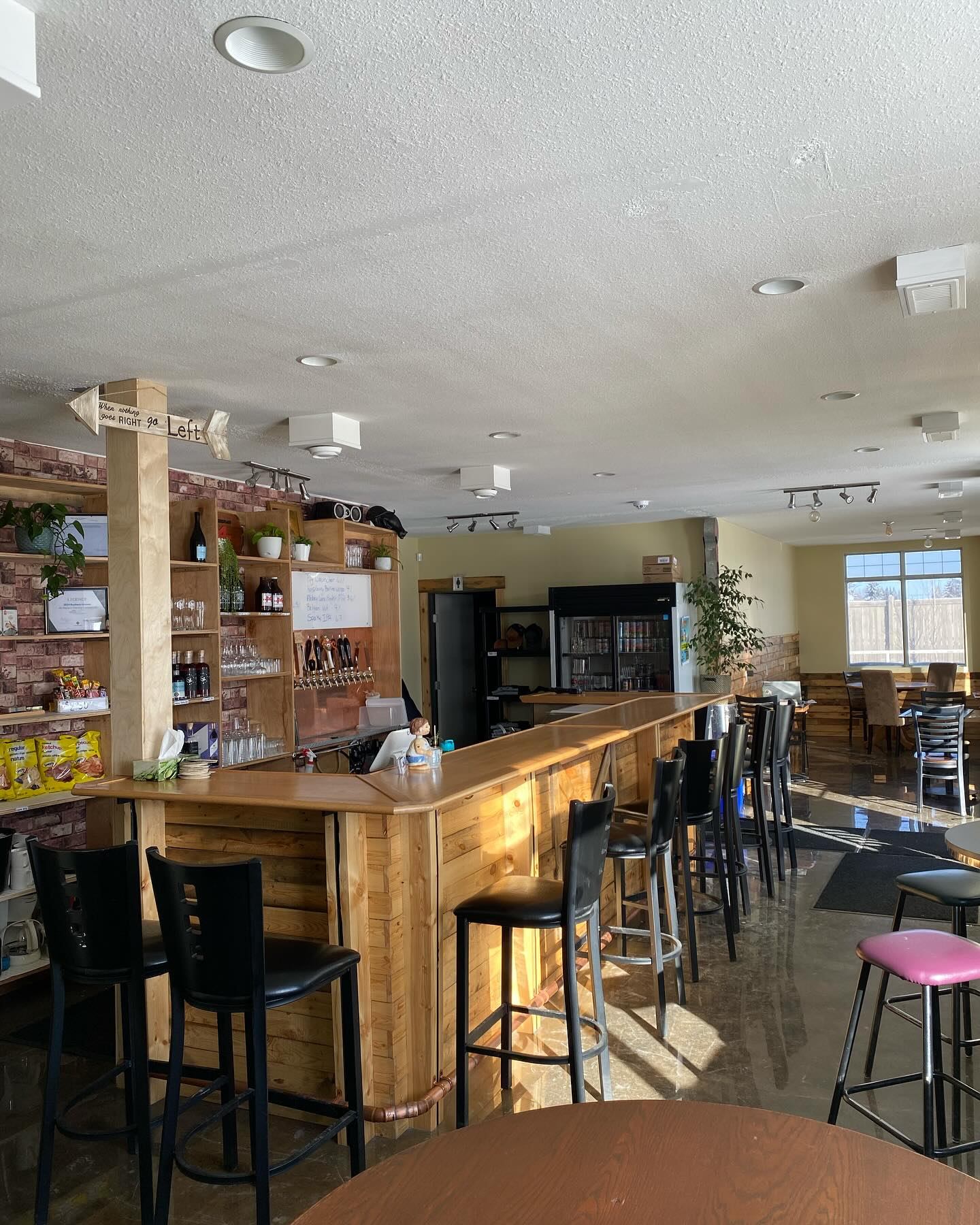 Wooden bar with high stools in bright café, shelves of snacks and drink taps.