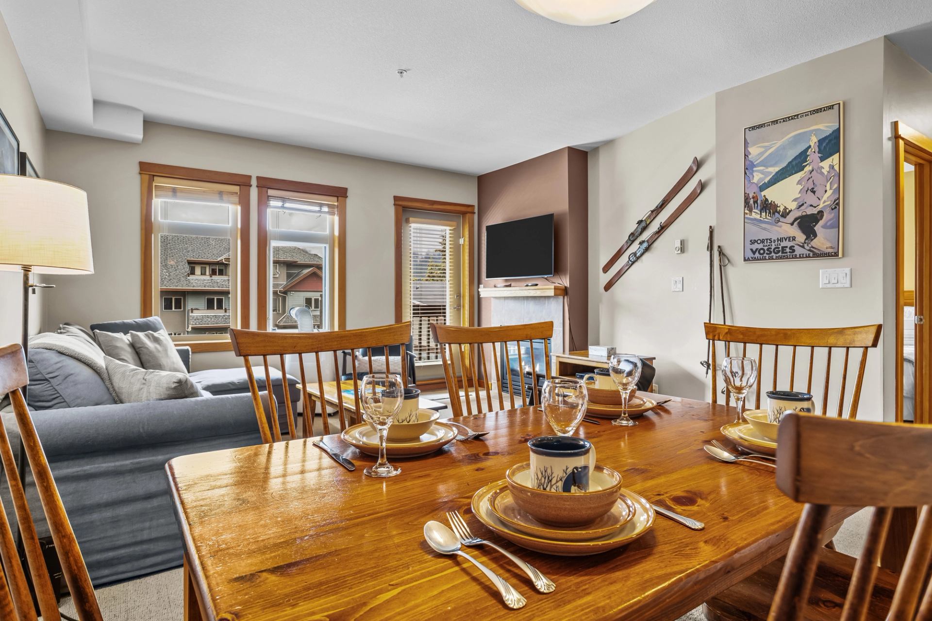 Dining table set with dishes beside a living room with fireplace and mounted skis.