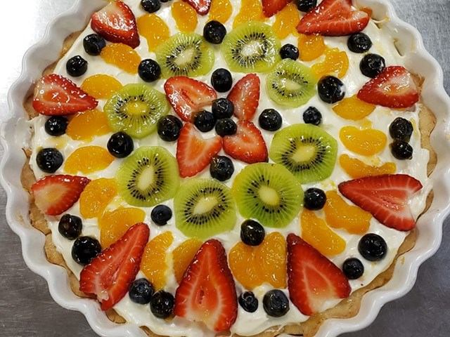 Colorful fruit tart with strawberries, kiwi, blueberries, and oranges in a white pan.