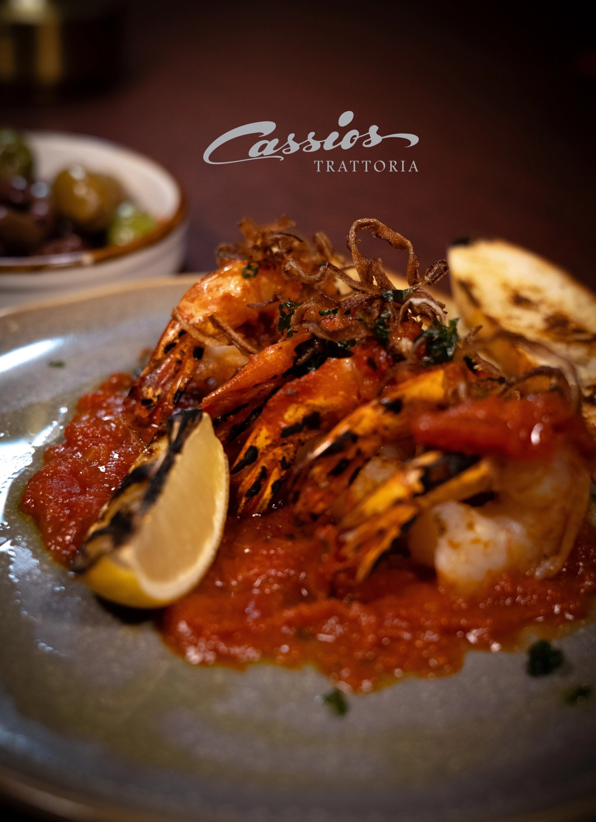 Grilled prawns on tomato sauce with charred lemon wedge at Cassios Trattoria.