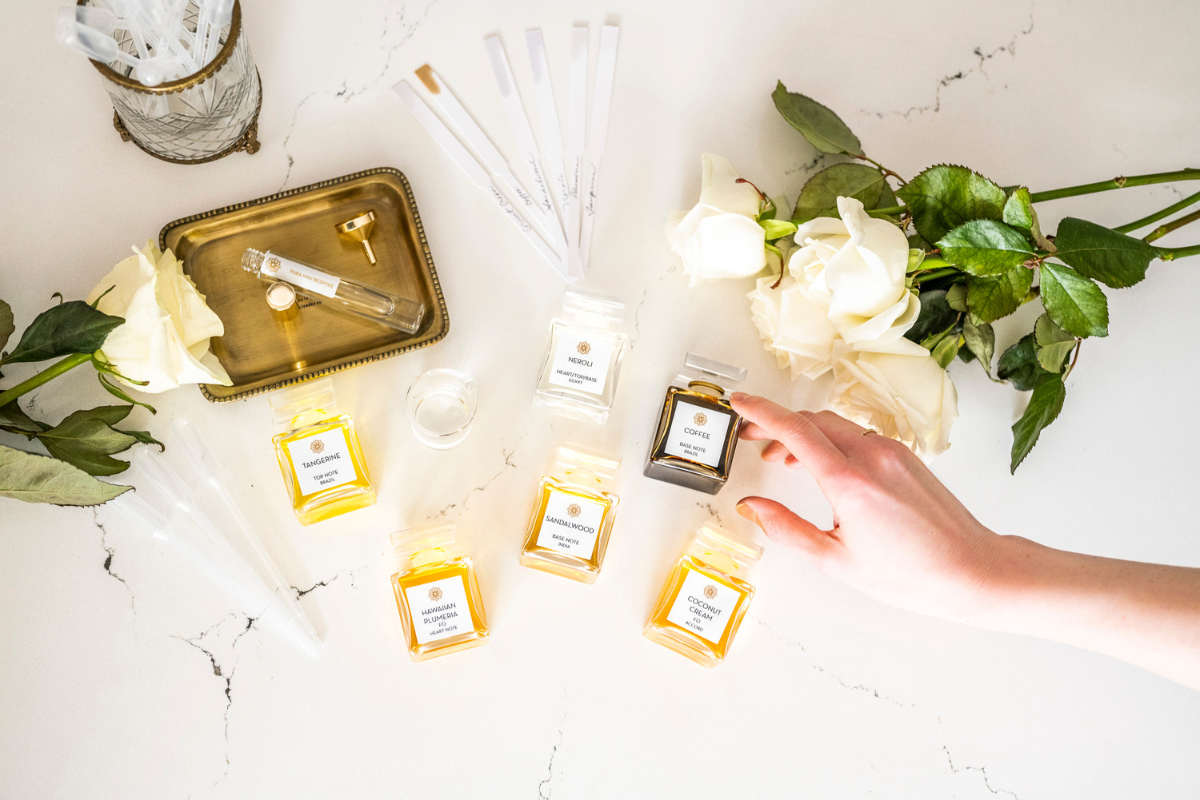 Perfume bottles, roses, and scent strips arranged on a table with a hand selecting a bottle.