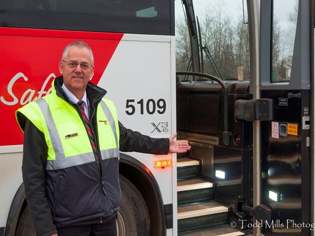Person in vest stands by open bus door with lit steps at Diversified Transportation.