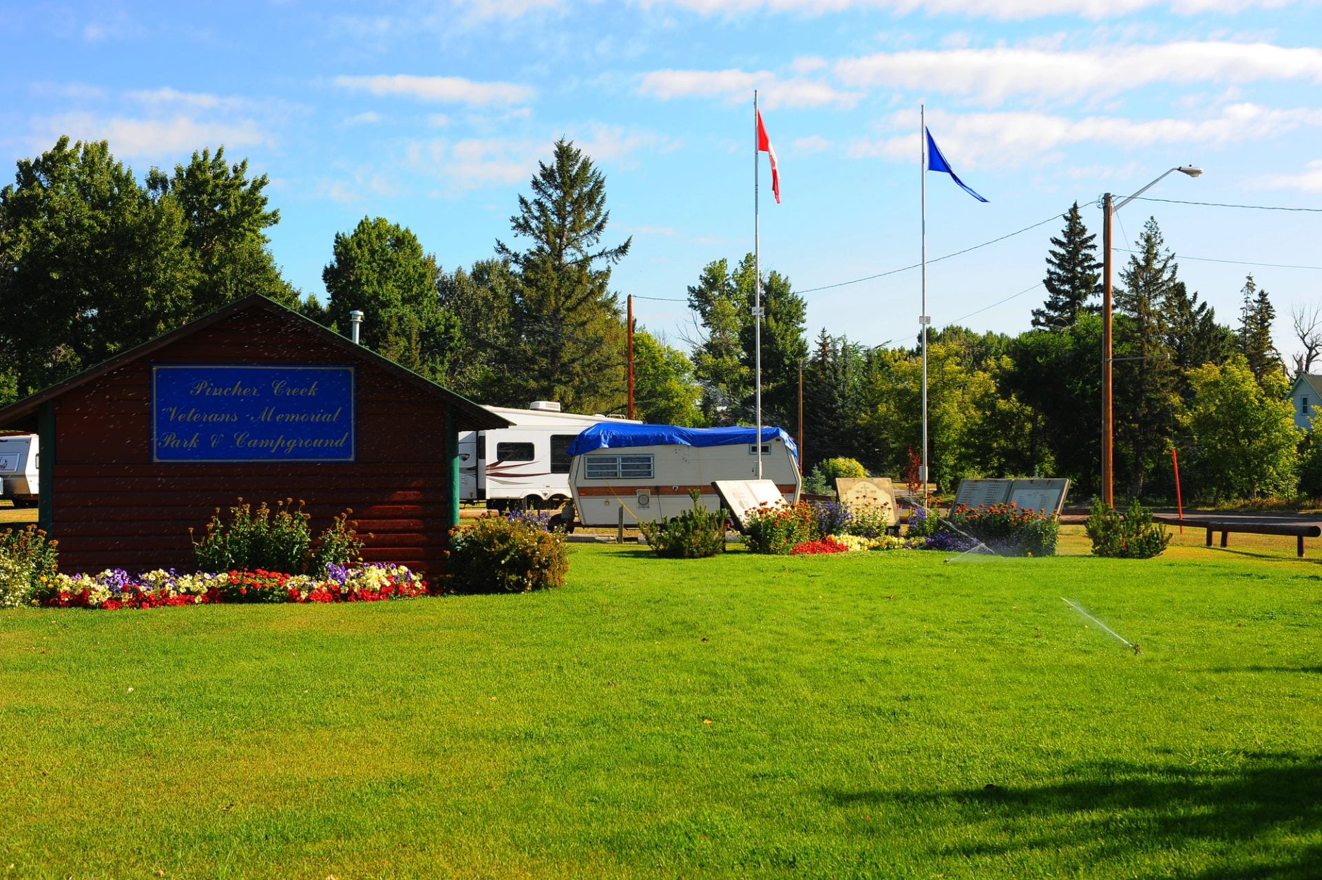 Campground with flower bed, wooden building, RVs, and Canadian flag.