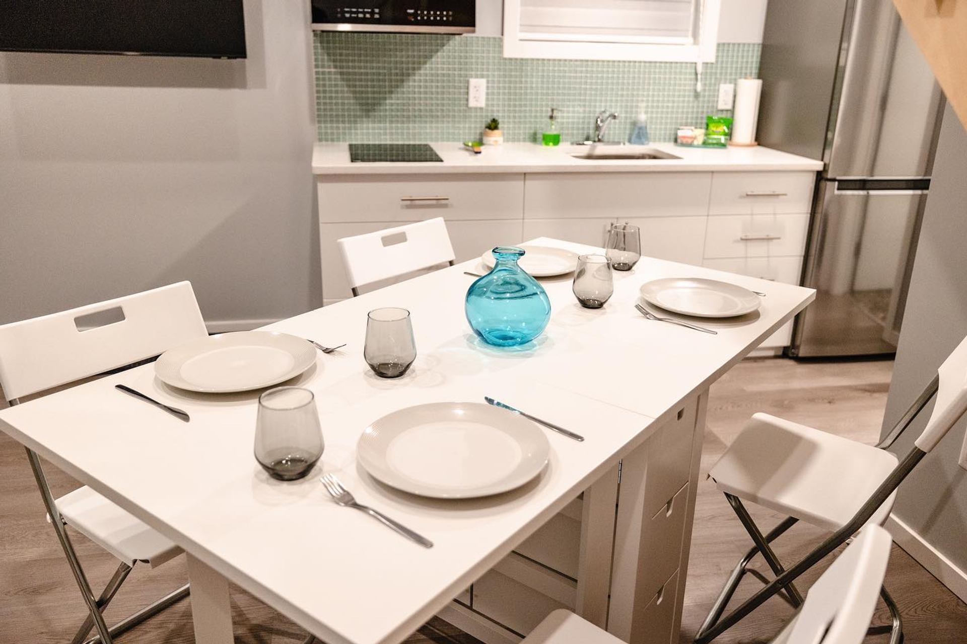 Kitchen dining table set with plates, glasses, and a blue vase in a modern bungalow.