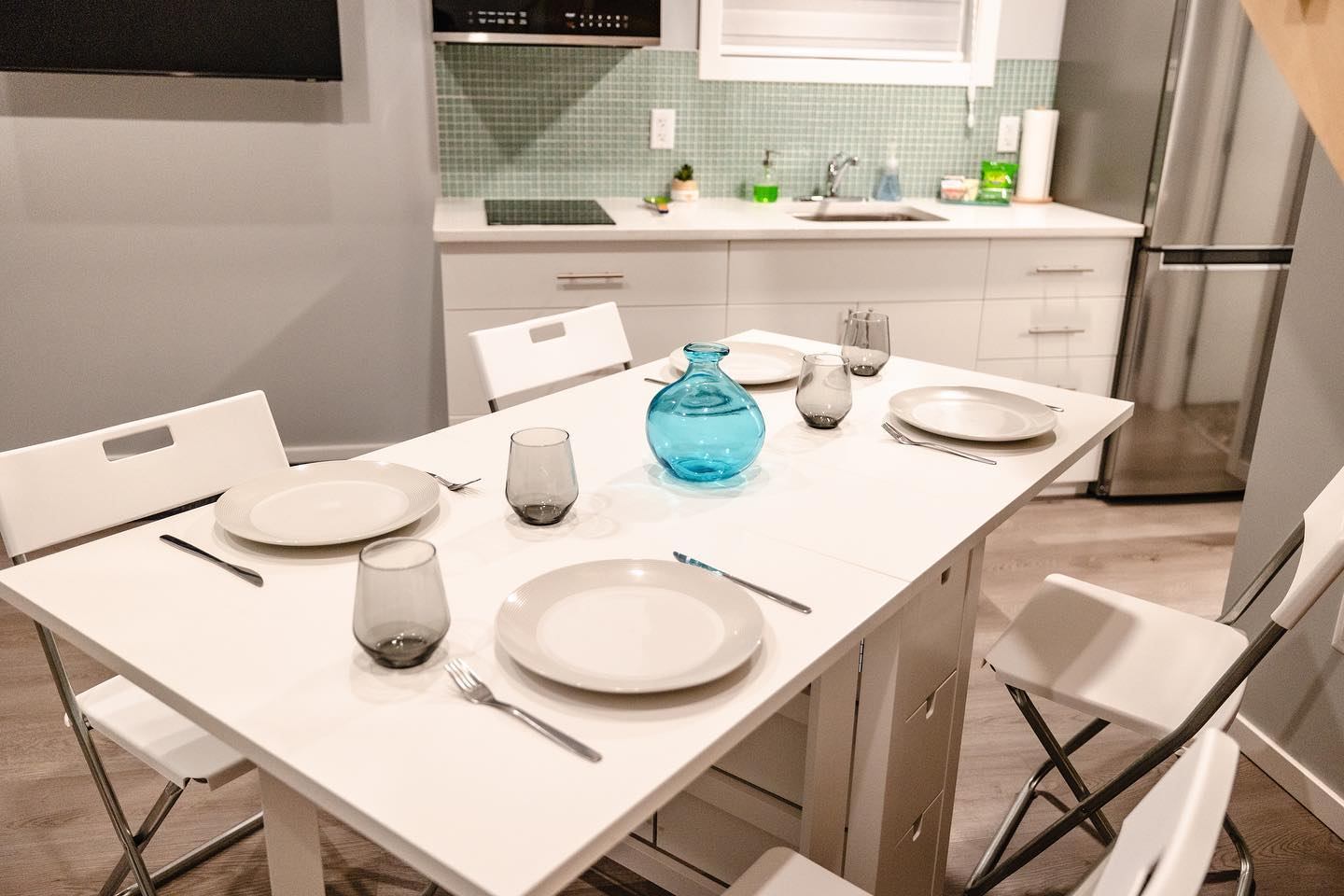 Kitchen dining table set with plates, glasses, and a blue vase in a modern bungalow.