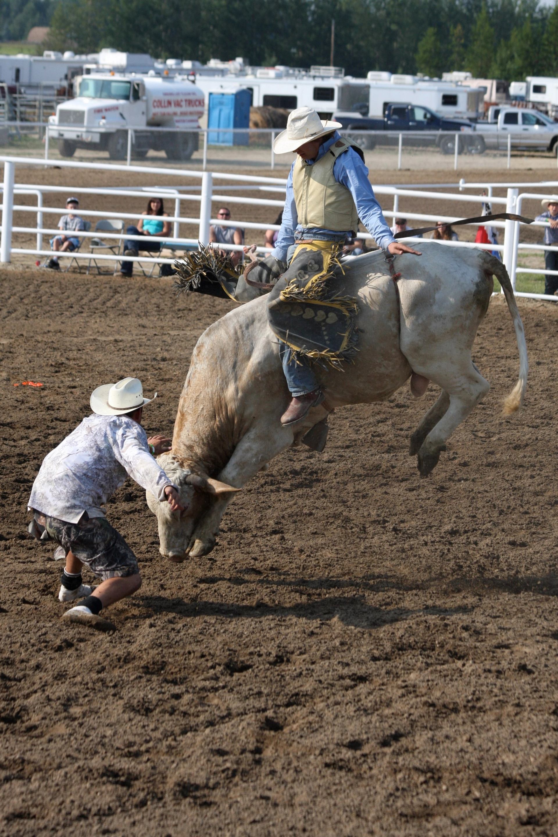 Rider holding on as a bucking bull leaps upward in a dirt arena.