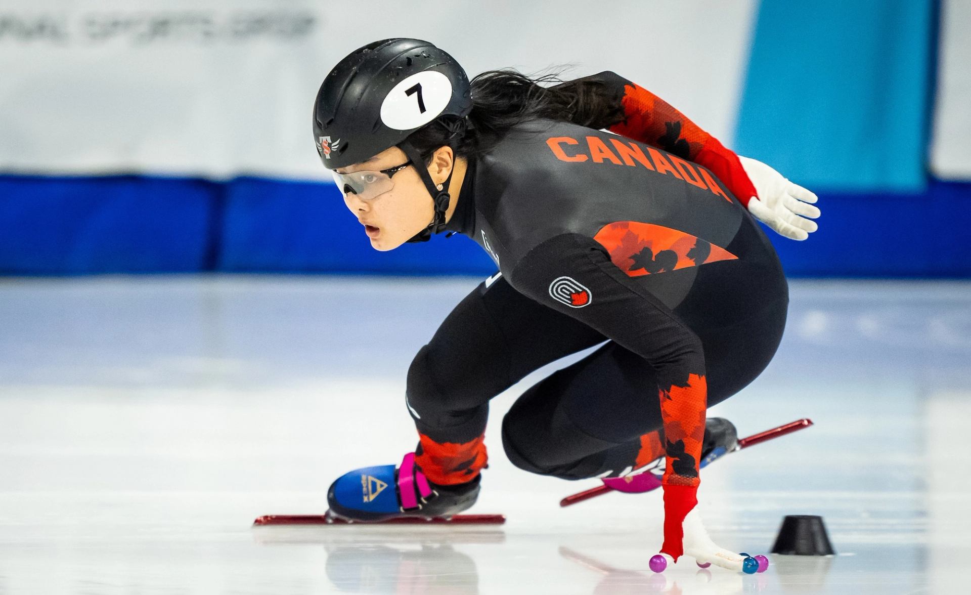 Canadian speed skater in action, leaning into a turn on the ice track.