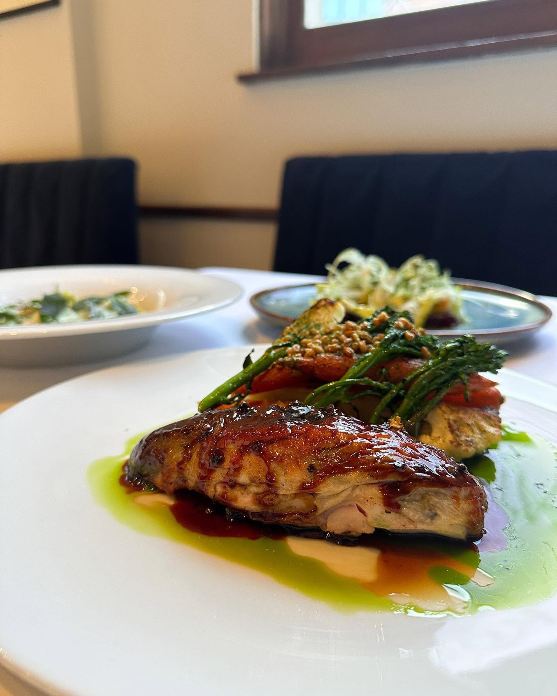 Roasted chicken breast with sauce and broccolini on white plate in restaurant.