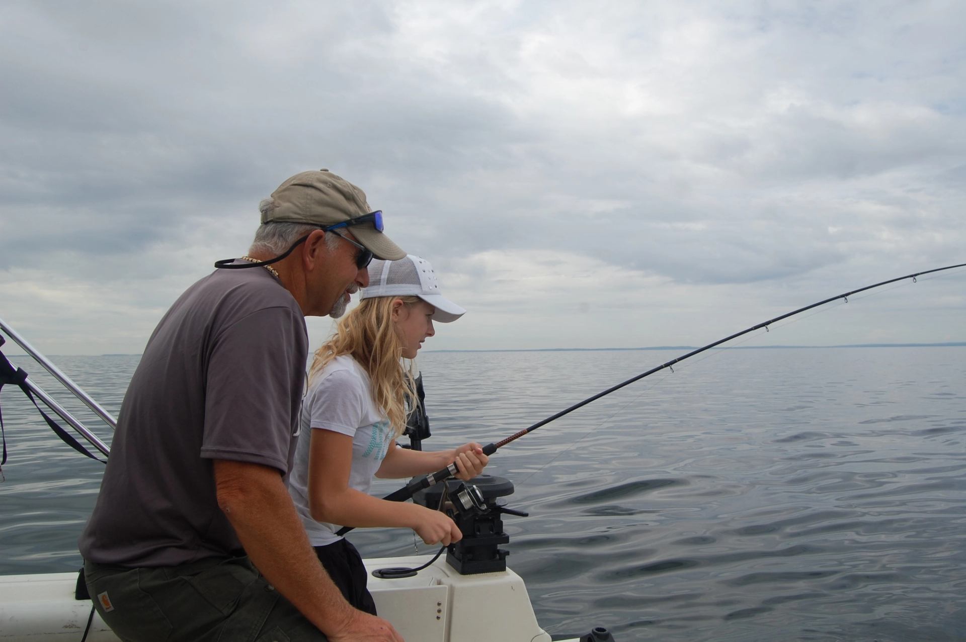 Two people fishing on a boat under a cloudy sky on calm waters.