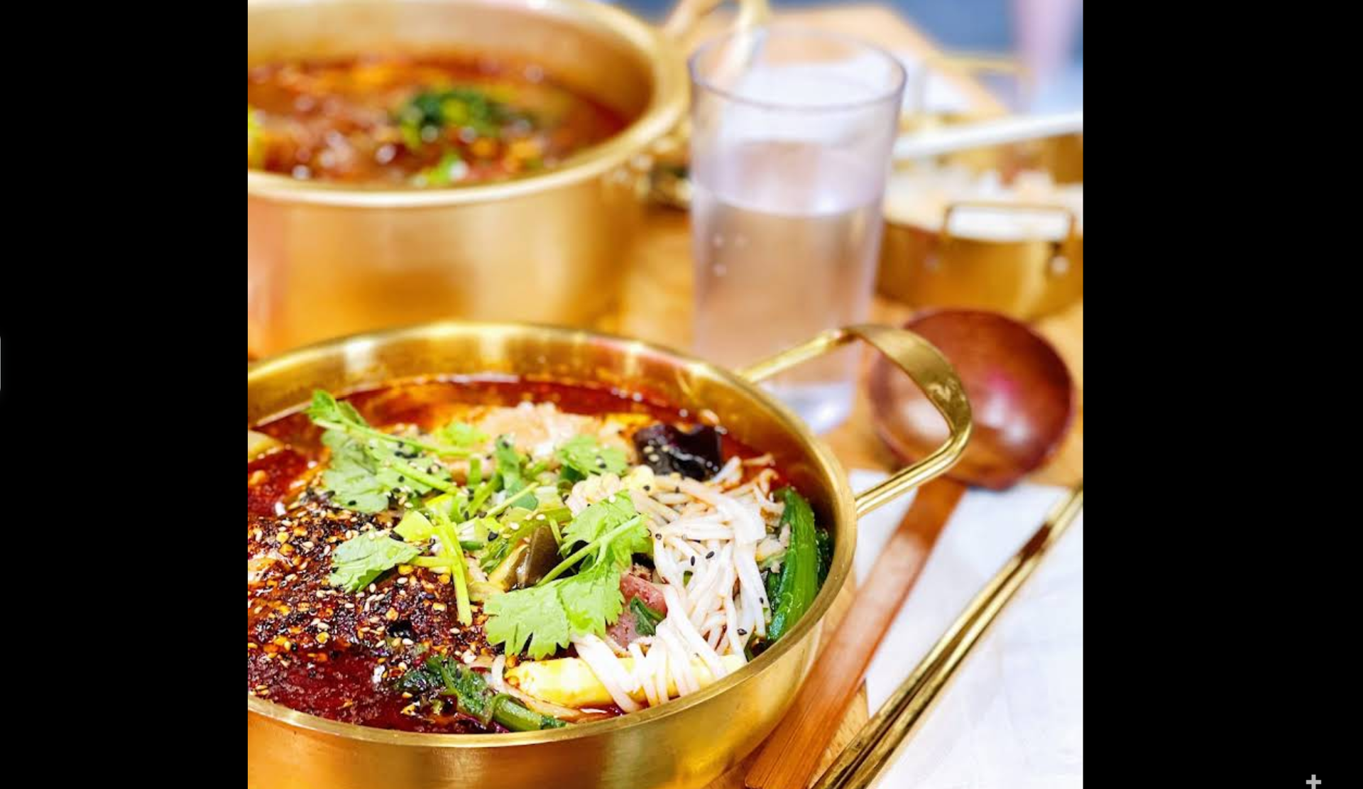 Golden pot of spicy soup with cilantro, bean sprouts, veggies, and a wooden spoon on the table.