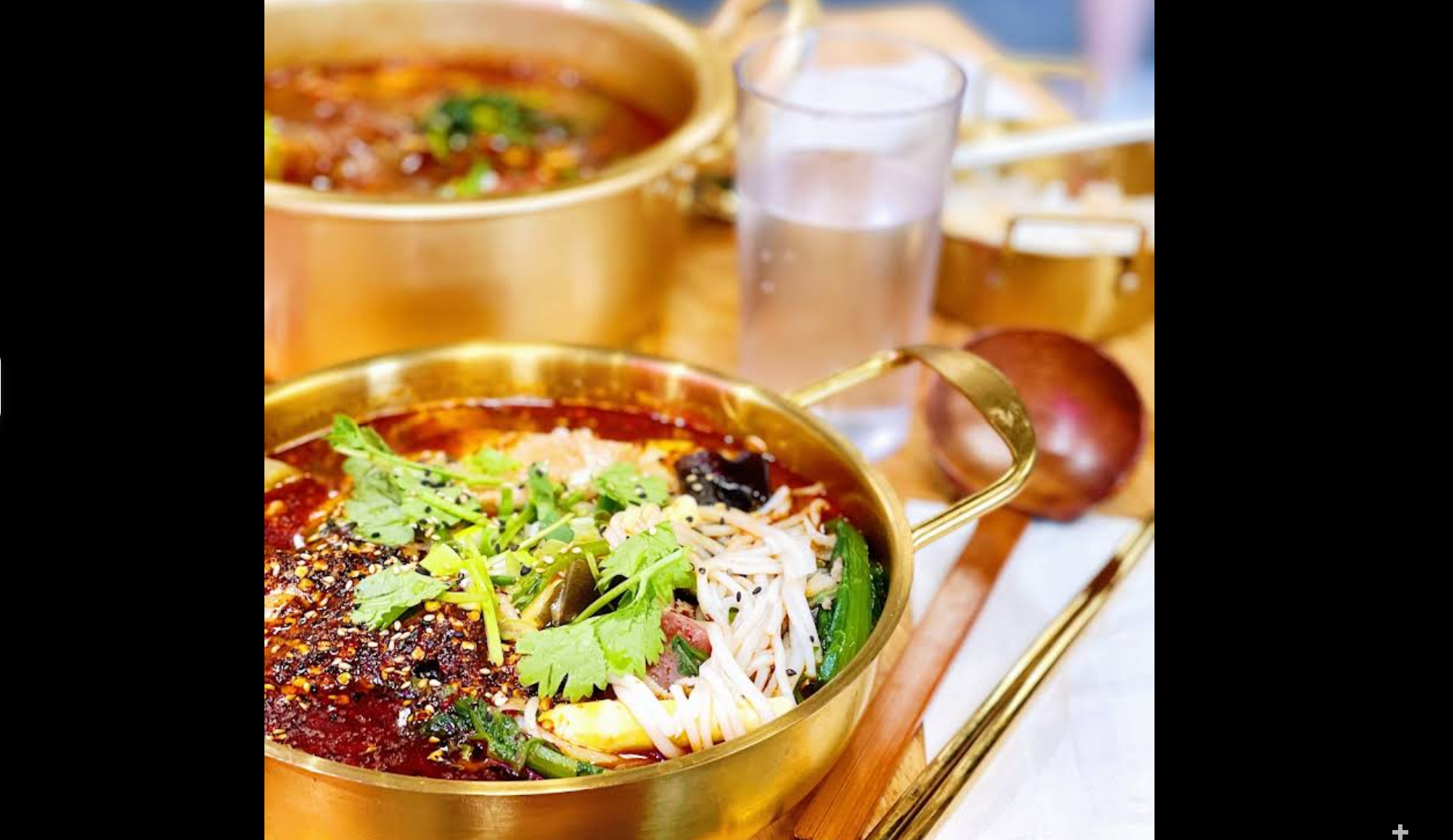 Golden pot of spicy soup with cilantro, bean sprouts, veggies, and a wooden spoon on the table.