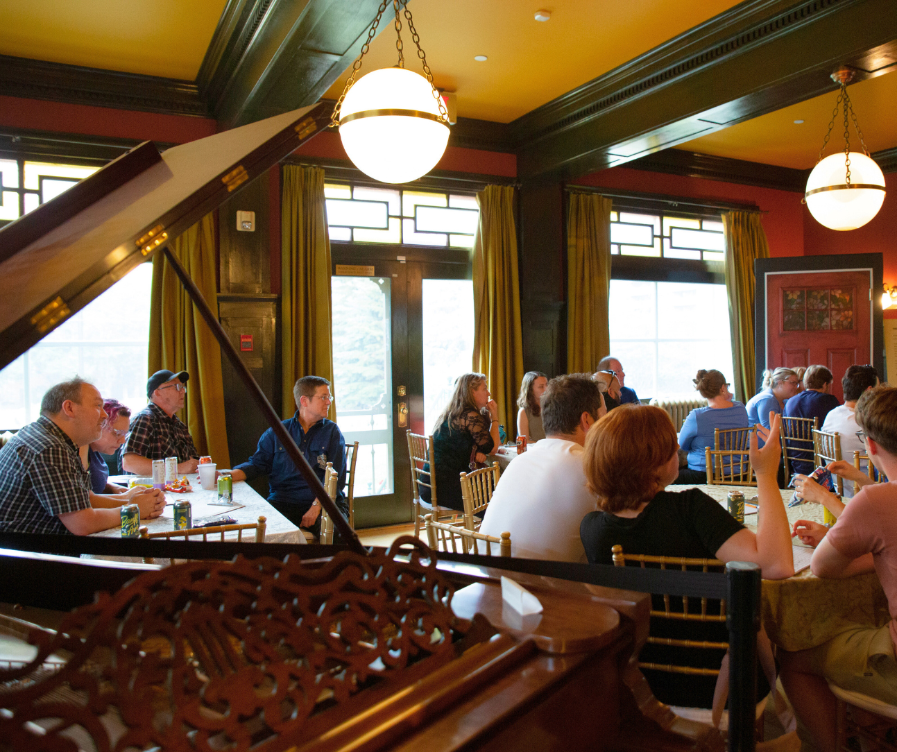 Elegant dining room with chandeliers, piano, and guests at tables.